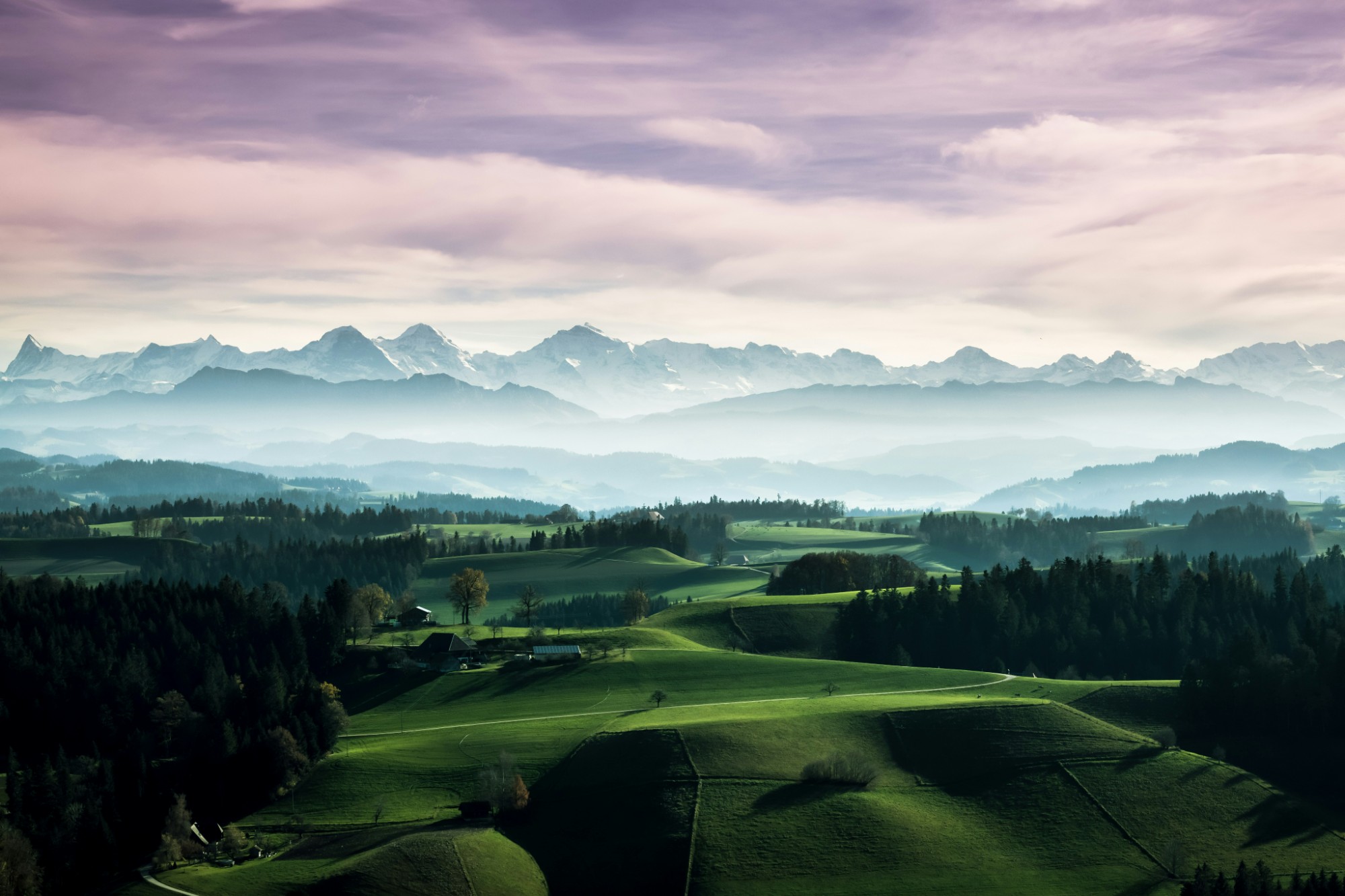 Schweizer Voralpenlandschaft mit grünen Hügeln und Alpenpanorama im Hintergrund.